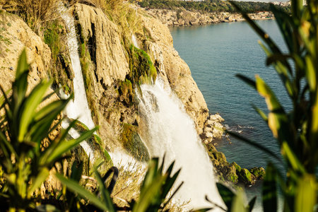 Majestic waterfall cascading over cliffs into the ocean surrounded by lush greenery.の写真素材