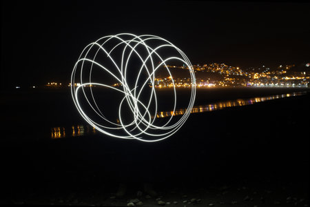 Abstract white light painting sphere on night beach with city background