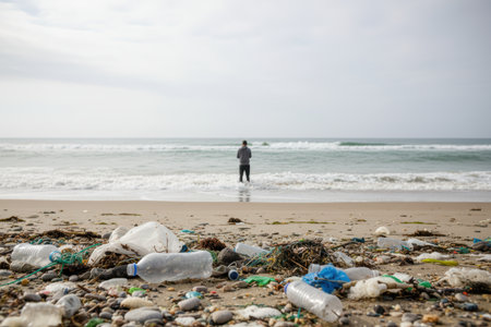 Plastic waste litters a beach where a man stands in the water.の素材