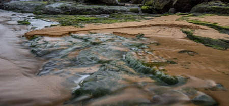 A long exposure composition of green rocks, sand & the water coming from the atlantic ocean at a beach in the Basque Country, Spainの写真素材