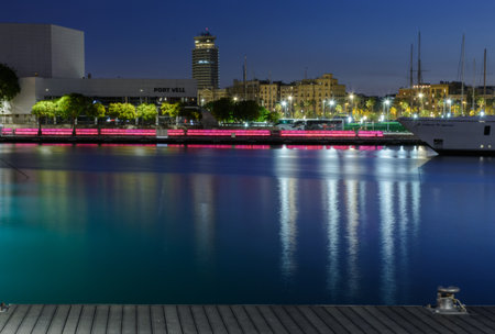 Summer scene of a harbor at night with a ship,buildings, the street lights & its reflection at...
