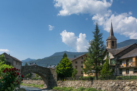 A lovely sunny day scene of a bridge above a river besides some home buildings & a bell tower at Esterri d'Aneu, Spainのeditorial素材