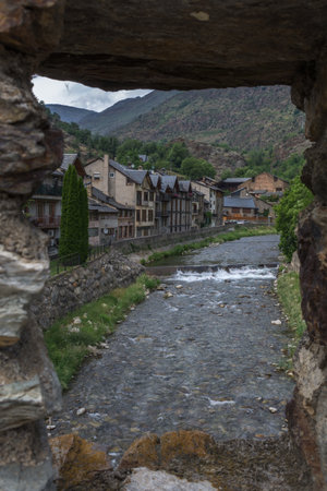 View of a river passing beside a village's homes seen through a window made of stone at Esterri d'Aneu, Spainのeditorial素材