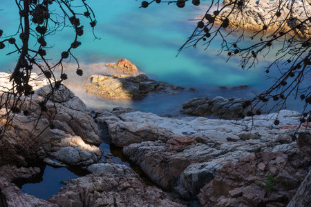 Mediterranean rocky formation next to emerald silky waters in front of some branches from above at...