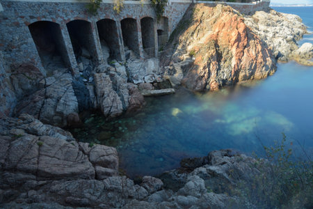 Arches construction close to a rocky coast next to a ladder all sunbathed with a morning sea at Platja d'Aro, spainの写真素材
