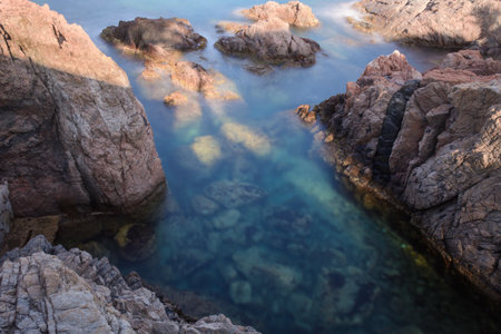 Translucent emerald waters of a little bay enlightened by the morning rays forging a whole rocky shore scene at Platja d'Aro, Spainの写真素材