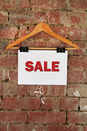 Sale sign hanging on coat hanger against rustic brick wallの写真素材