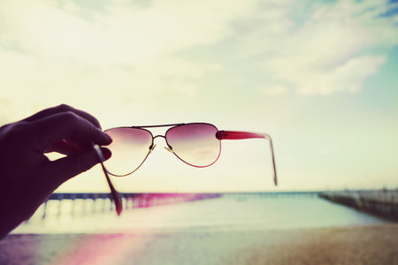 Colorful light leaks on hand holding sunglasses at a beach on vacationの写真素材