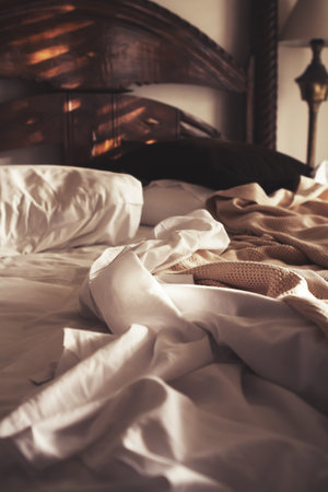 Morning sunlight on an unmade luxury bed of white sheets and beige blanketの写真素材