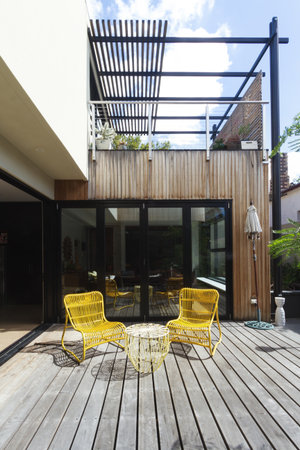 Pair of yellow cane outdoor chairs on wooden deck in contemporary courtyard