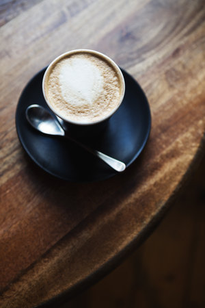 Overhead view of cafe latte in black ceramic cup on a wooden restaurant tableの写真素材