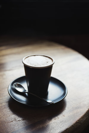 Moody restaurant setting with cafe latte by window light on rustic wooden tableの写真素材