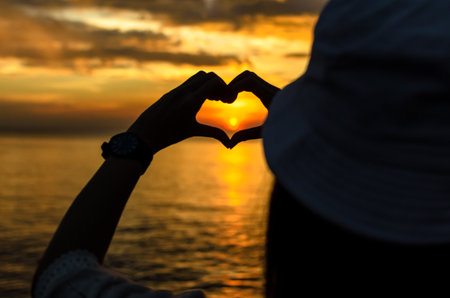 Sunset of love in the heart hand on the sea with silhouette.の写真素材
