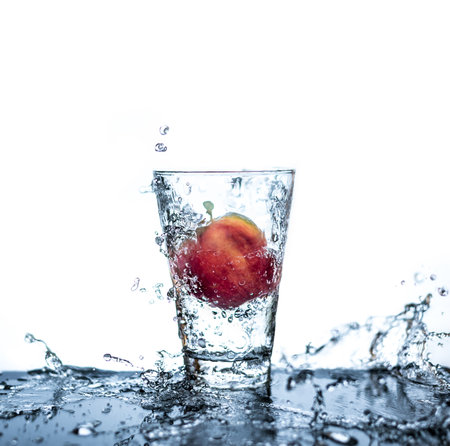Red apple has droping to the glass and splashing water around the glass and on the table with reflection and isolated white background.の写真素材