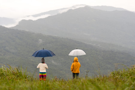 Duo female hiker holding umbrella and relaxing with big mountain and heavy mist under the cloudy sky.の写真素材
