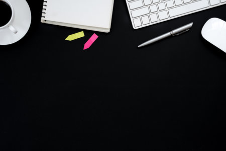 Office desk table with computer, white mouse, silver pen, pink and green sticky note and black...