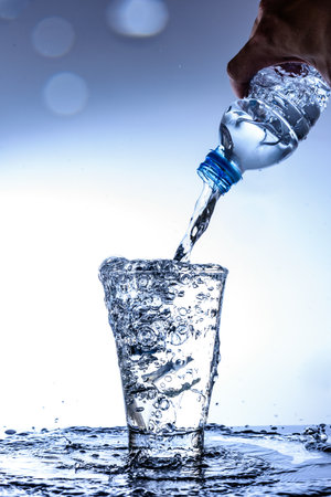 Pouring water and splashing in the glass with reflection on mirror.