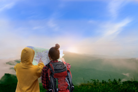 Two girls look at the map with mountain and blue sky background in the morning and think how to go....