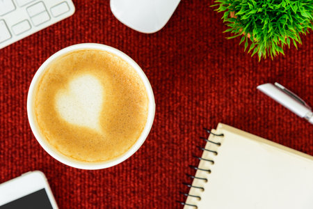 A latte coffee with art heart milk on the red desk table from top view and copy space. Flat lay with desk, business and valentine concept.の写真素材