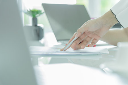 Hand of businesswoman writing on paper with silver pen and pointing on documents in the office interriorの写真素材
