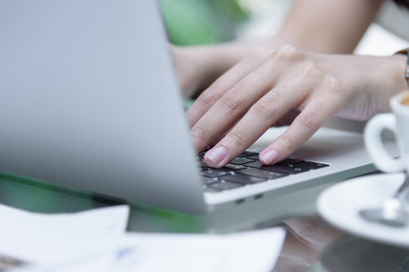 Asian woman hands has touching and typing on laptop computer with blurred coffee, computer and view...