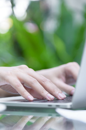 Asian woman hands has touching and typing on laptop computer with blurred coffee, computer and view outside window.の写真素材