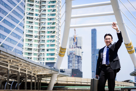 The asian businessman has holding a black bag and making hello gesture.