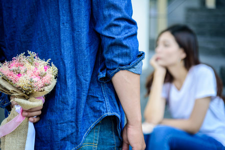 Asian man has preparing and waiting with flower for say sorry and apologies to girlfriend.の写真素材
