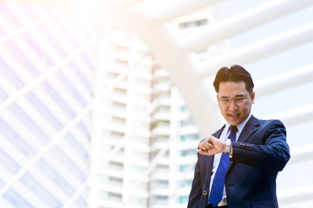 The asian businessman has holding a black bag and looking on watch in hurrying time.の写真素材