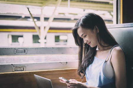 Asian woman traveler has working with laptop and phone inside the train at Hua Lamphong station at Bangkok, Thailand.の写真素材