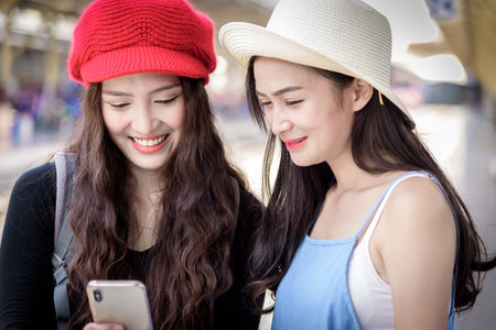 Asian women traveler have playing a mobile phone and talking for waiting the train with happiness at Hua Lamphong station at Bangkok, Thailand.の写真素材