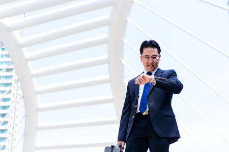 The asian businessman has holding a black bag and looking on watch in hurrying time.の写真素材