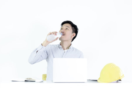 Asian employee engineer salary man sitting at desk and drinking water, isolated on white background.の写真素材