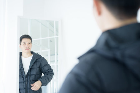 Asian handsome man looking at himself in mirror indoorsの写真素材