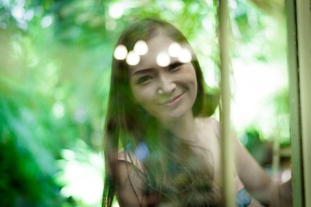 Asian pretty girl has relaxing behind blurred mirror with happy and smiling at Little Tree Garden cafe, Nakhon Pathom province, Thailand in the morning.の写真素材