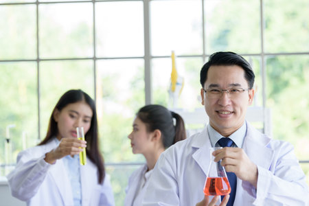 Asian senior laboratory scientist man working at lab with asian young student scientist backgroud.の写真素材