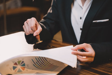 A seal to show approval of an agreement or contract by an authorized person. A businesswoman is about to stamp a document at the office legally. The boss signs the certificate or letter on the desk.の写真素材