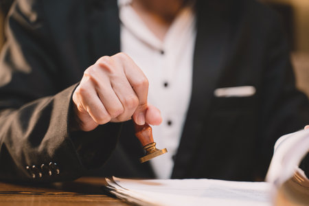 A seal to show approval of an agreement or contract by an authorized person. A businesswoman is about to stamp a document at the office legally. The boss signs the certificate or letter on the desk.の写真素材