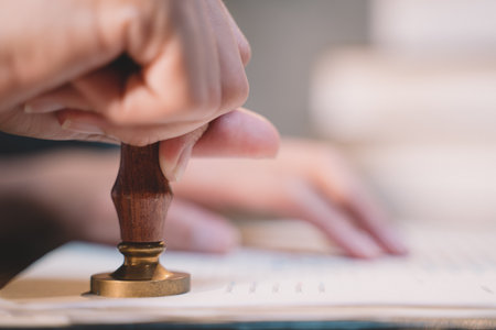 A seal to show approval of an agreement or contract by an authorized person. A businesswoman is about to stamp a document at the office legally. The boss signs the certificate or letter on the desk.の写真素材