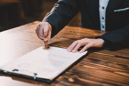 A seal to show approval of an agreement or contract by an authorized person. A businesswoman is about to stamp a document at the office legally. The boss signs the certificate or letter on the desk.の写真素材