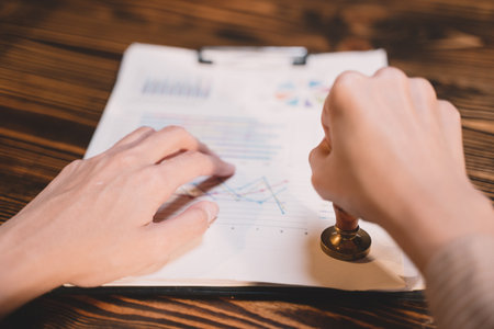 A seal to show approval of an agreement or contract by an authorized person. A businesswoman is about to stamp a document at the office legally. The boss signs the certificate or letter on the desk.の写真素材