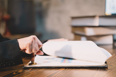 A seal to show approval of an agreement or contract by an authorized person. A businesswoman is about to stamp a document at the office legally. The boss signs the certificate or letter on the desk.の写真素材