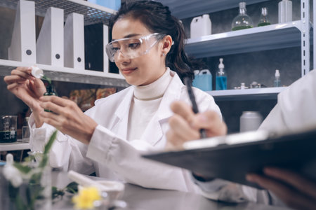 Researcher woman are drop a liquid to a bottle in her hand and researcher man are look to substance and note to notebook in his hand at laboratory.の写真素材