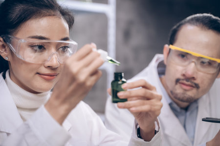 Researcher woman are drop a liquid to a bottle in her hand and researcher man are look to substance and note to notebook in his hand at laboratory.の写真素材