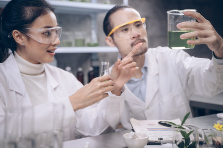 Two research people are comparing and discuss information at beaker in their hands at cosmetic lab. They are smile and happy in their research.の写真素材