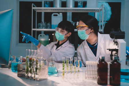 2 scientists are analyzing data eco skin care beauty products in nighttime laboratory development concept, research with plants and scientific extraction in glassware, Alternative green herb medicine for body health careの写真素材