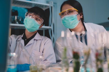 2 scientists are analyzing data eco skin care beauty products in nighttime laboratory development concept, research with plants and scientific extraction in glassware, Alternative green herb medicine for body health careの写真素材