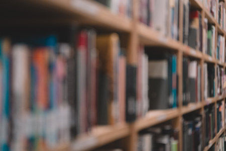 In the quiet interior of the university library, rows of blurry bookcases stretch across the empty room, filled with literature and textbooks offering knowledge for research and learning in various fields of study.の写真素材