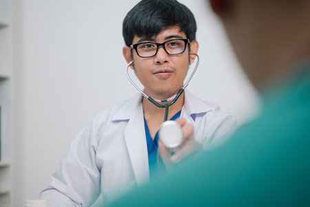 In the bustling hospital, the doctor used a stethoscope to listen to the patient's heartbeat during the exam, focusing on health care strategies to combat the disease in cardiology.の写真素材