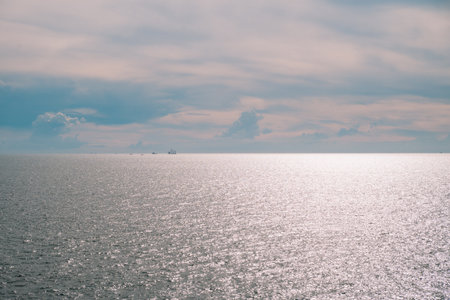 Blue water stretches to the horizon where sea and sky meet, clouds drifting gently as sunlight dances on the ocean, creating a breathtaking natural landscape.の写真素材
